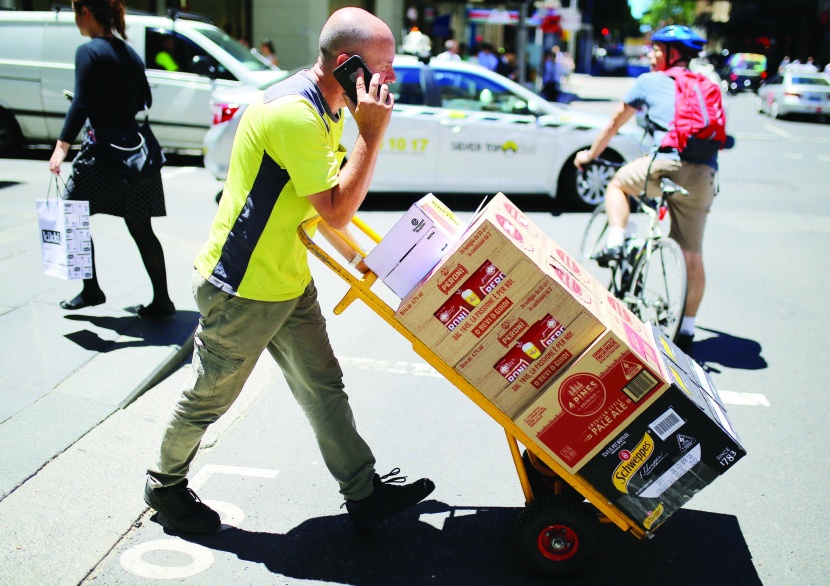 عامل يدفع عربة محملة بالبضائع عبر طريق رئيسي وسط سيدني