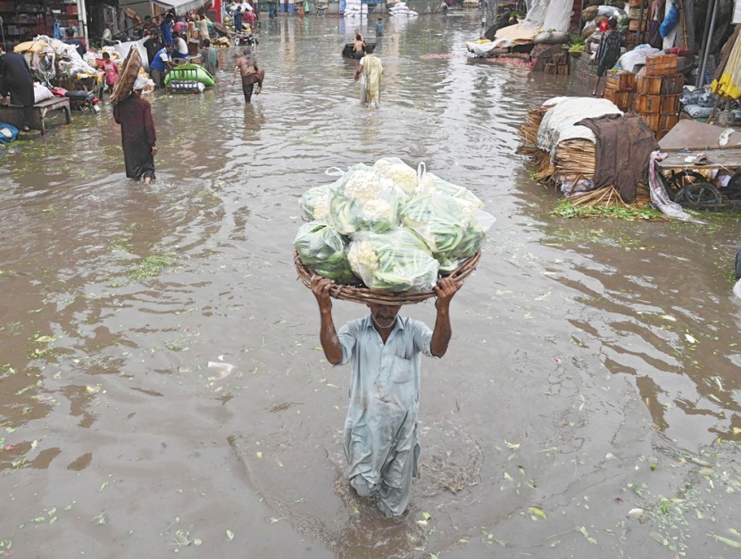 بائع يحمل سلة محملة بالخضراوات وسط شارع غمرته المياه بعد هطول أمطار موسمية غزيرة في لاهور