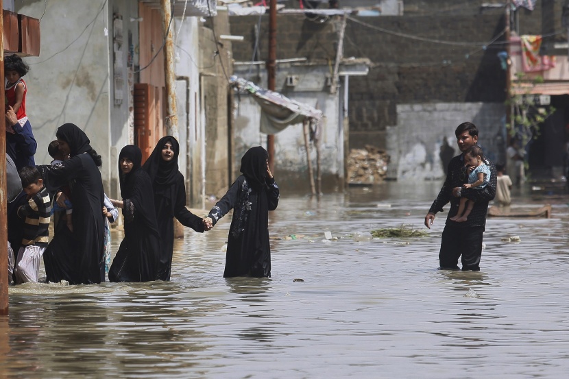  عائلات باكستانية تجازف بخوض شارع غمرته المياه بعد هطول أمطار غزيرة في مدينة كراتشي .