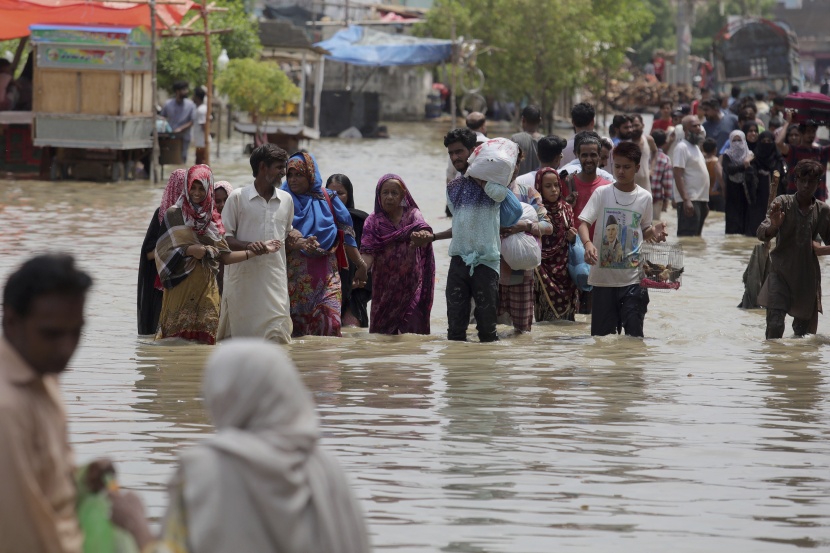  عائلات باكستانية تجازف بخوض شارع غمرته المياه بعد هطول أمطار غزيرة في مدينة كراتشي .