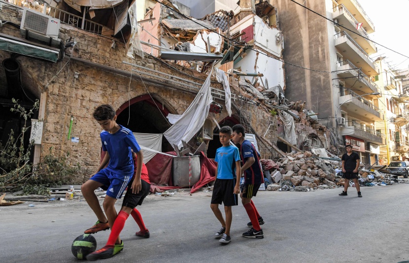 أطفال يلعبون كرة القدم وسط شارع خلفه الدمار بعد انفجار بيروت 