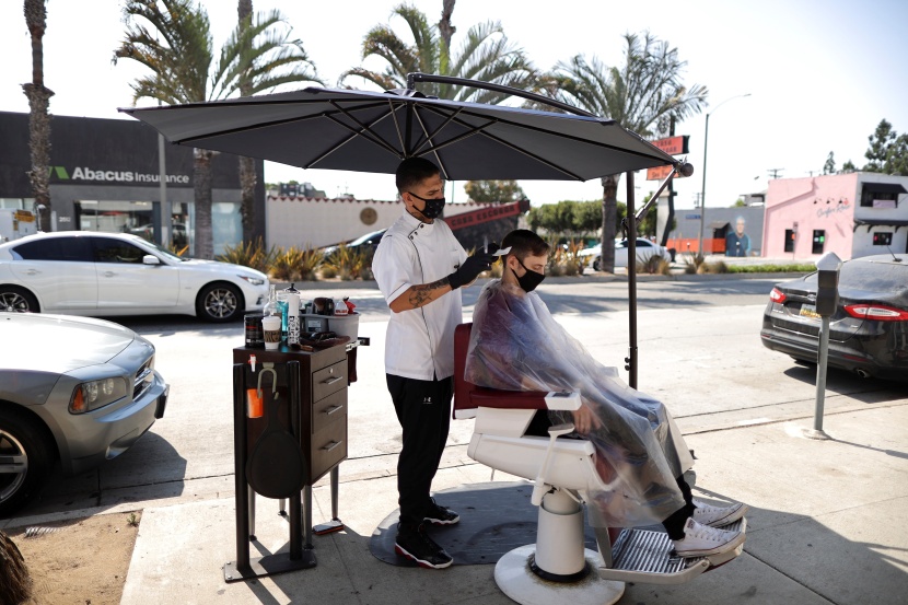  حلاق يؤدي عمله على قارعة الطريق بعد إغلاق محله بسبب إجراءات كورونا الاحترازية المنفذة في سانتا مونيكا الأمريكية.