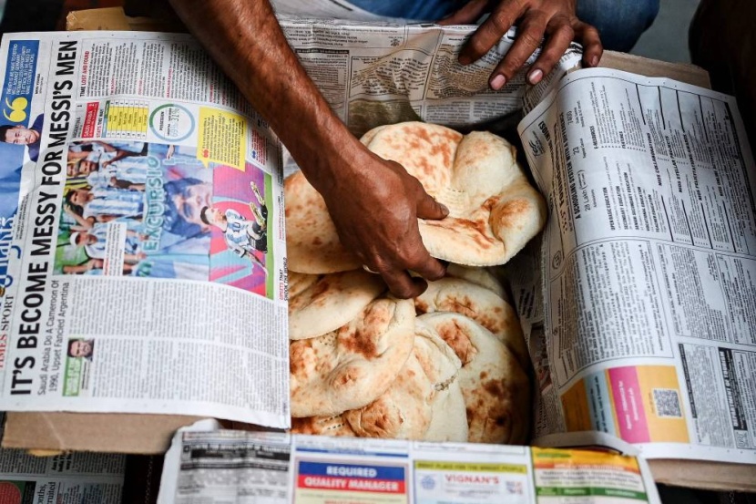 عامل يضع خبز «الروتي» في ورق صحف تغطي نهائيات كأس العالم