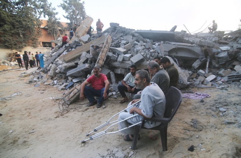 فلسطينيون يجلسون بجوار مبنى دمرته غارة جوية إسرائيلية في غزة